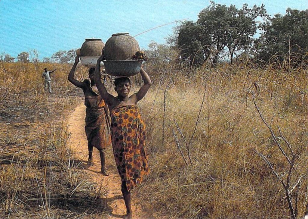 Women carrying pots on their head as they walk through a narrow road